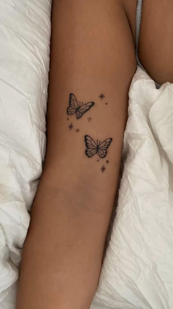 Two black butterfly tattoos with small star accents on a person's inner forearm