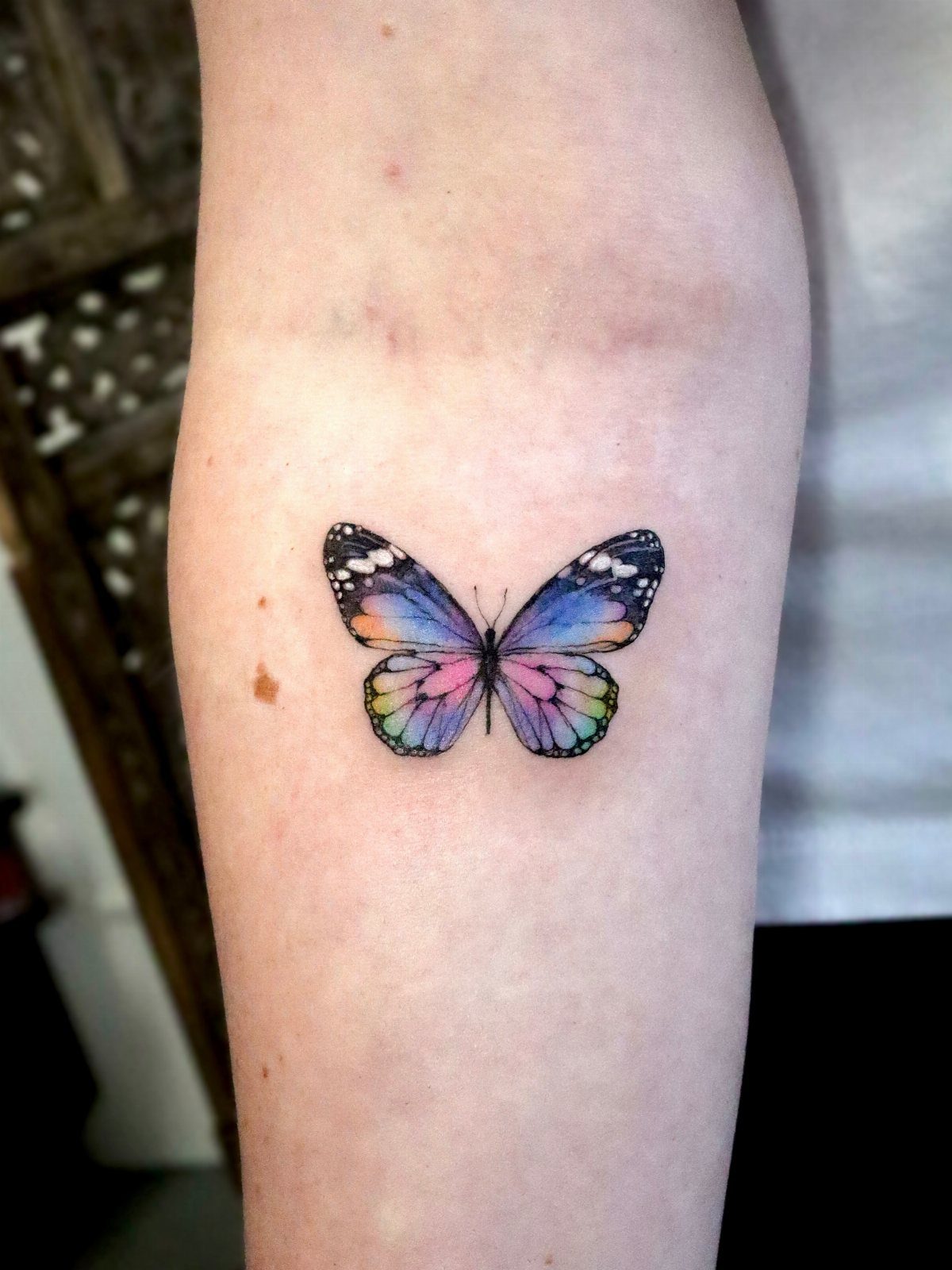 Colorful butterfly tattoo with blue and purple wings on a person's forearm