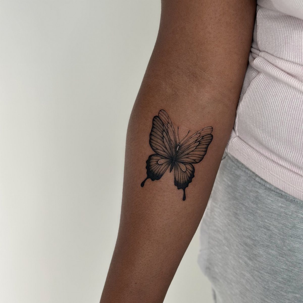 Black ink butterfly tattoo with detailed wings on a person's upper arm