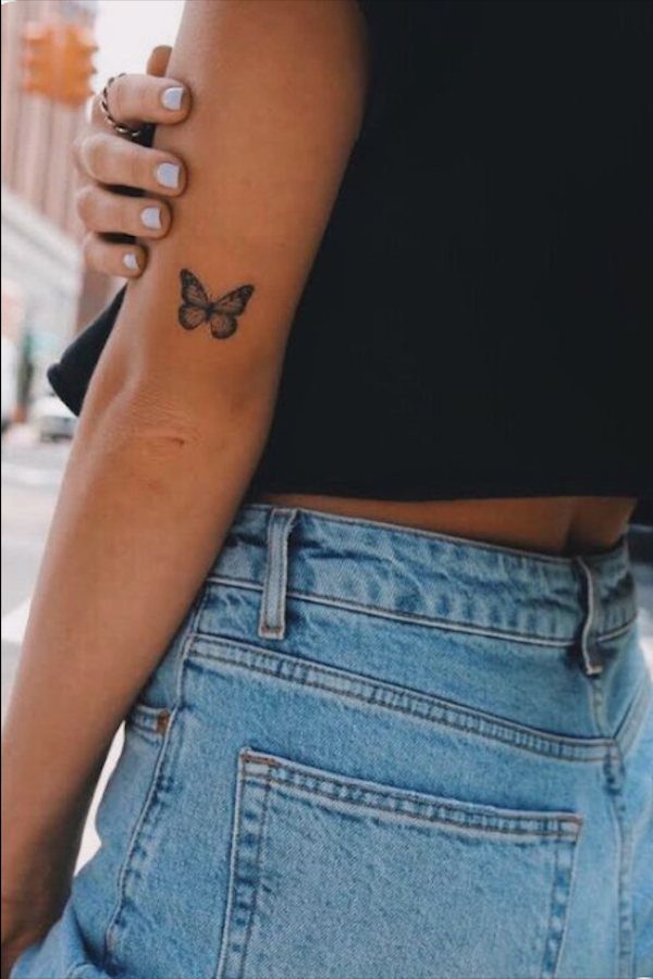 Small black ink butterfly silhouette tattoo on the upper inner arm of a person.