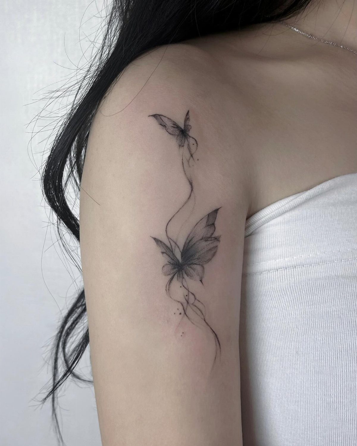 Two black ink butterfly tattoos on an upper arm connected by a flowing line