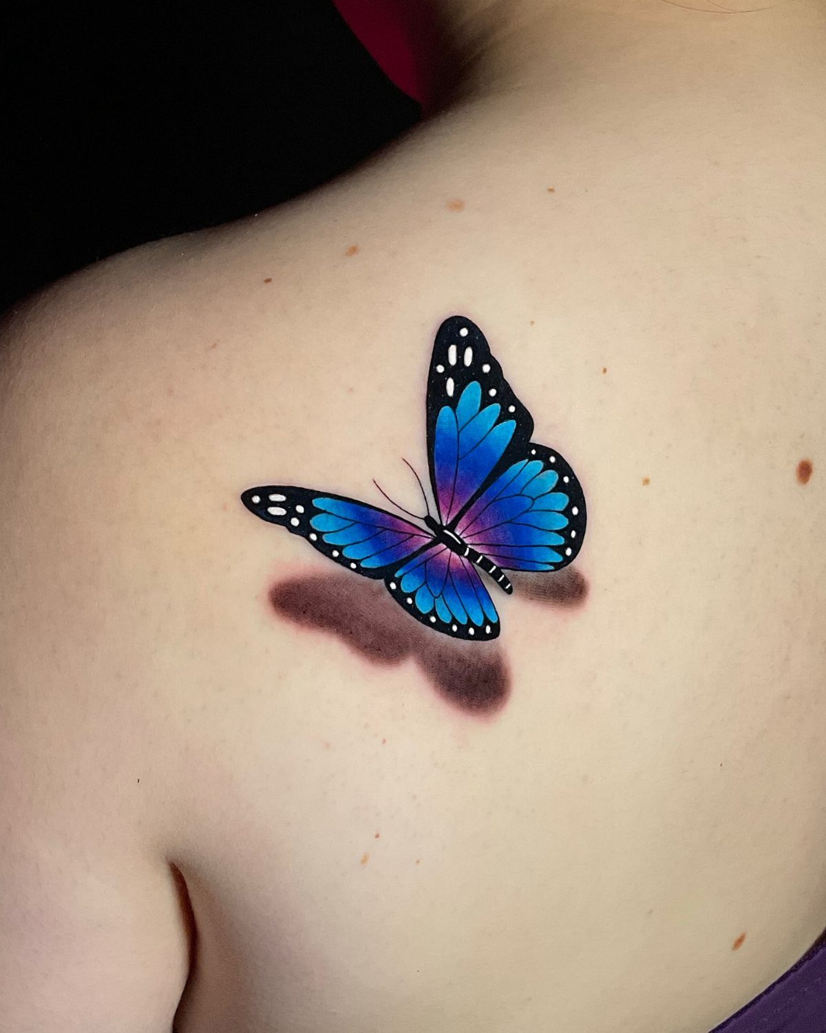 Blue and purple butterfly tattoo on a back with a realistic drop shadow.