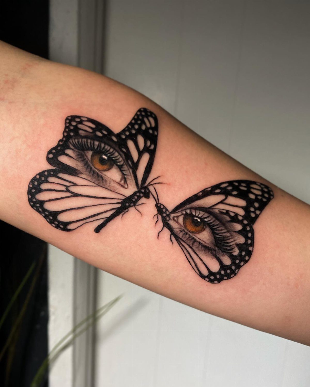 Two butterfly tattoos on a forearm with realistic human eyes in the wings
