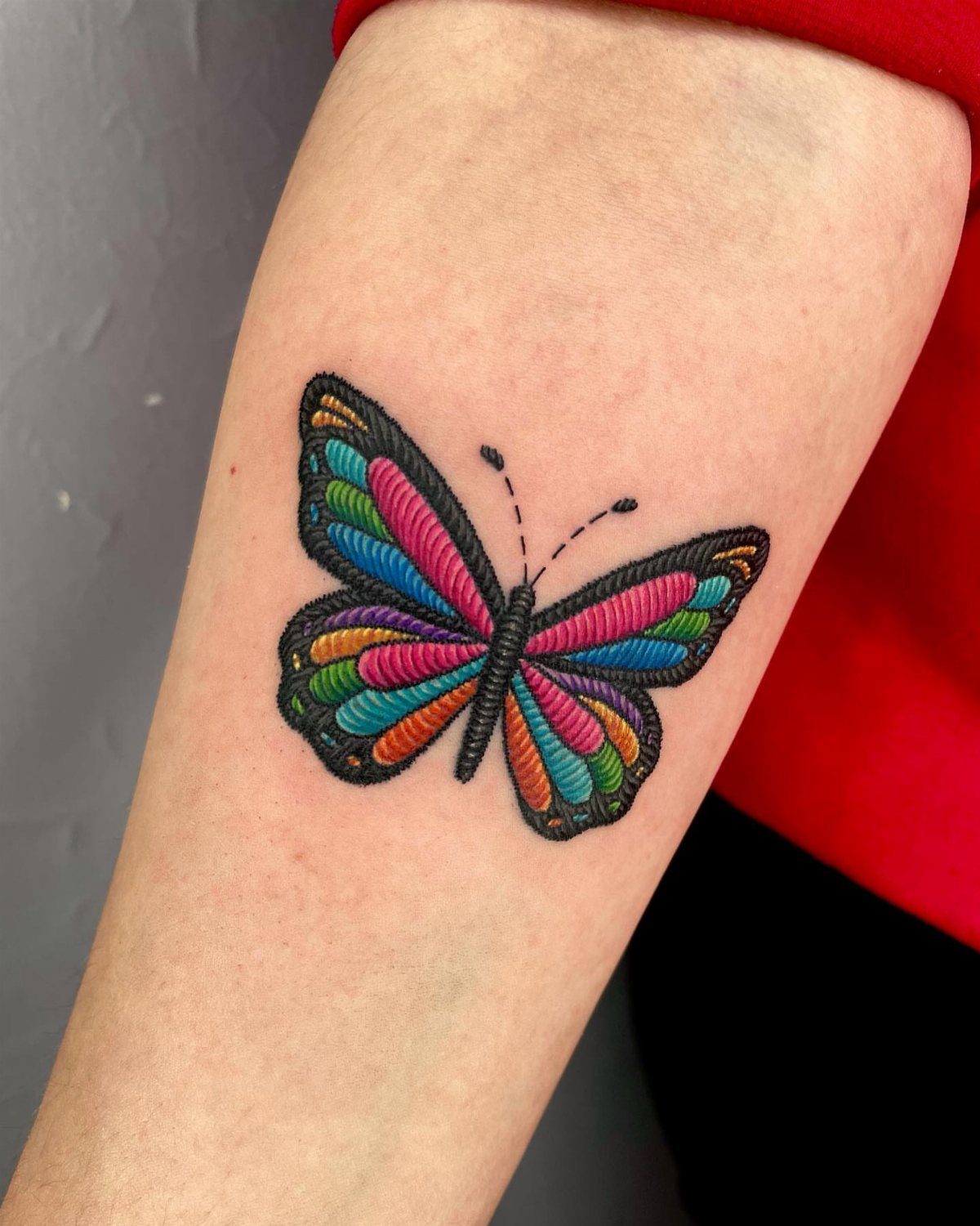 Colorful butterfly tattoo with blue, pink, and orange wings on a forearm