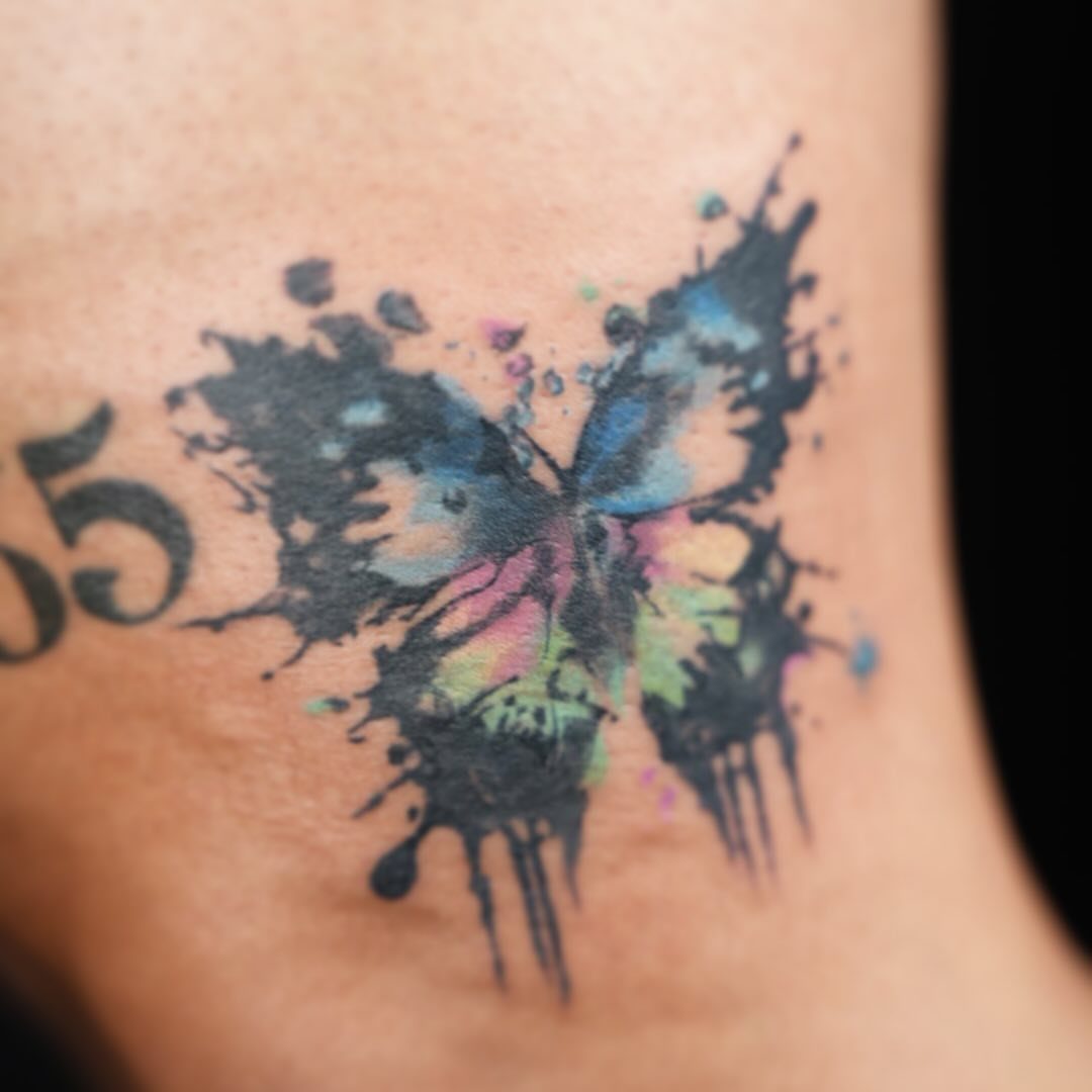 Butterfly tattoo with colorful ink splashes and splatters on human skin