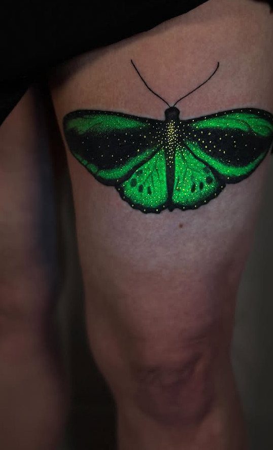 Green and black butterfly tattoo with detailed wings on a person's thigh
