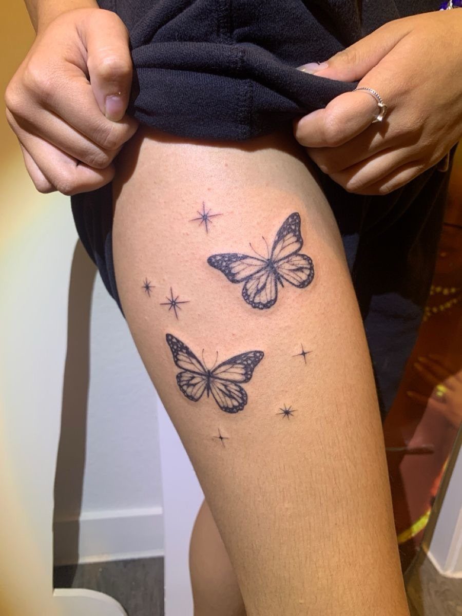 Two black ink butterfly tattoos with stars on a person's upper thigh