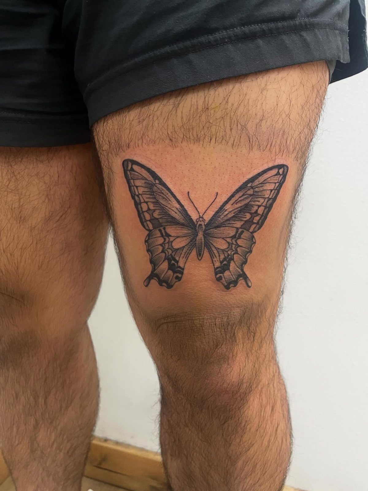 Black ink butterfly tattoo centered on a person's upper leg above the knee