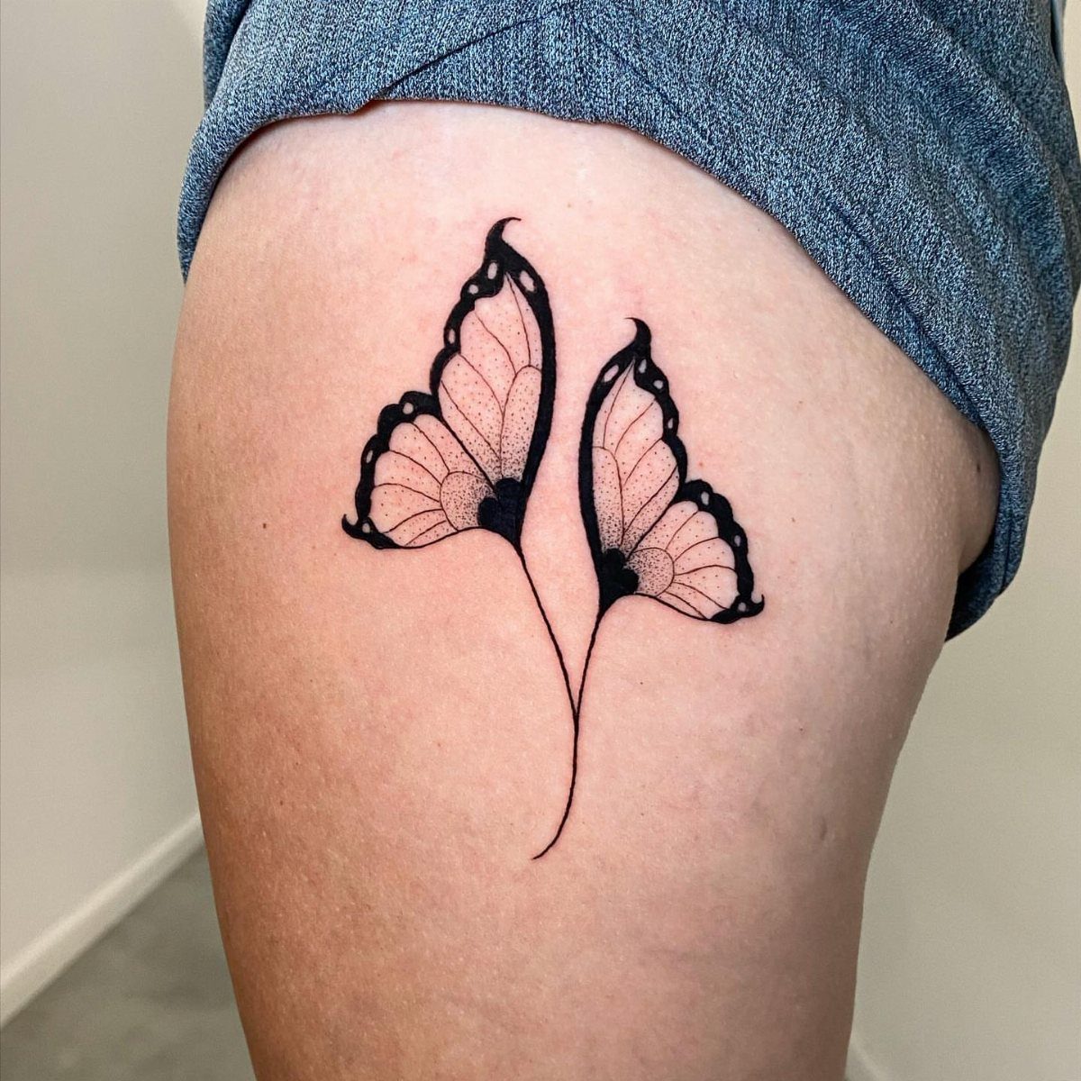 Two stylized butterfly wings tattooed in black ink on a person's upper thigh.