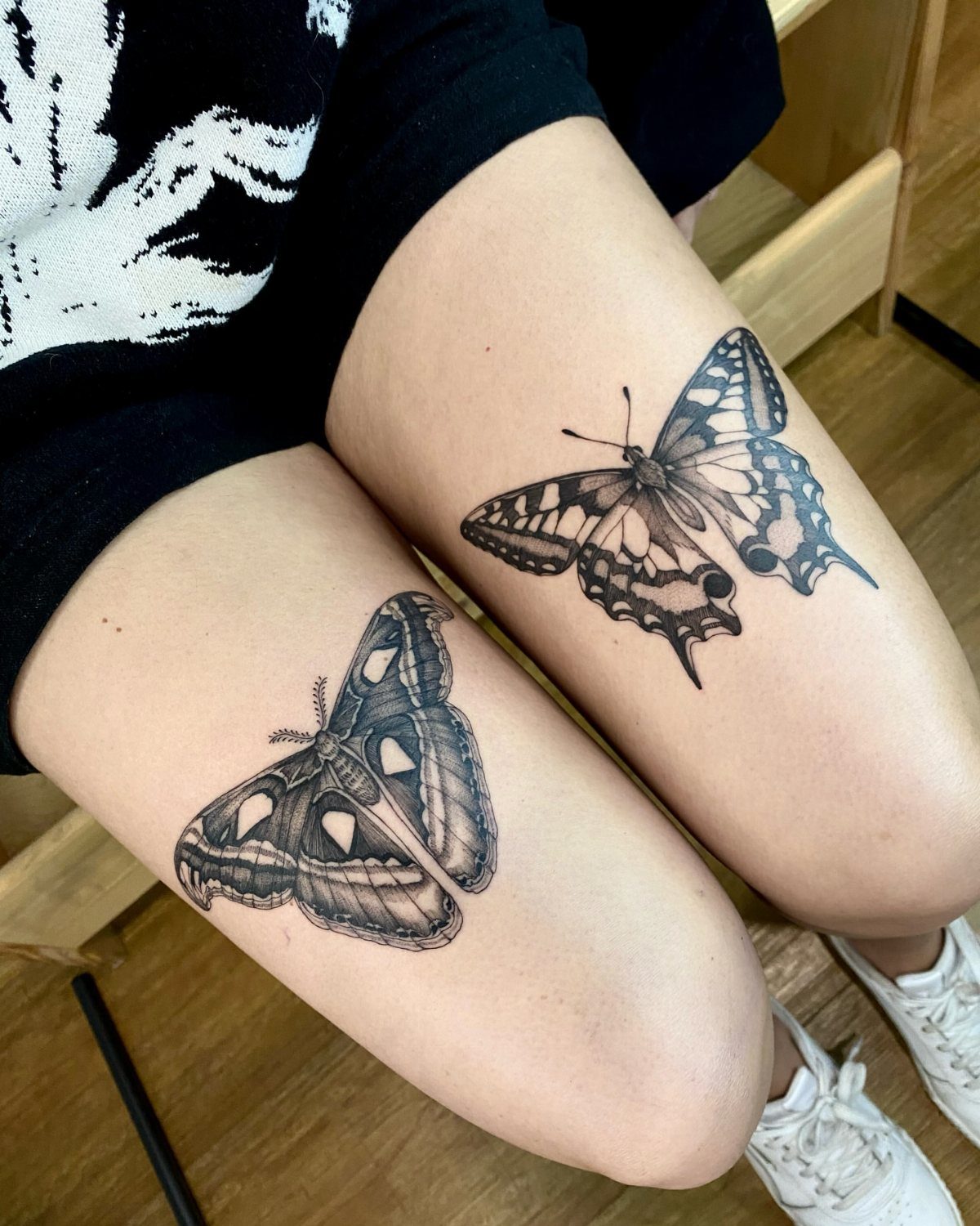Blackwork butterfly and moth tattoos on the upper thighs of a person.