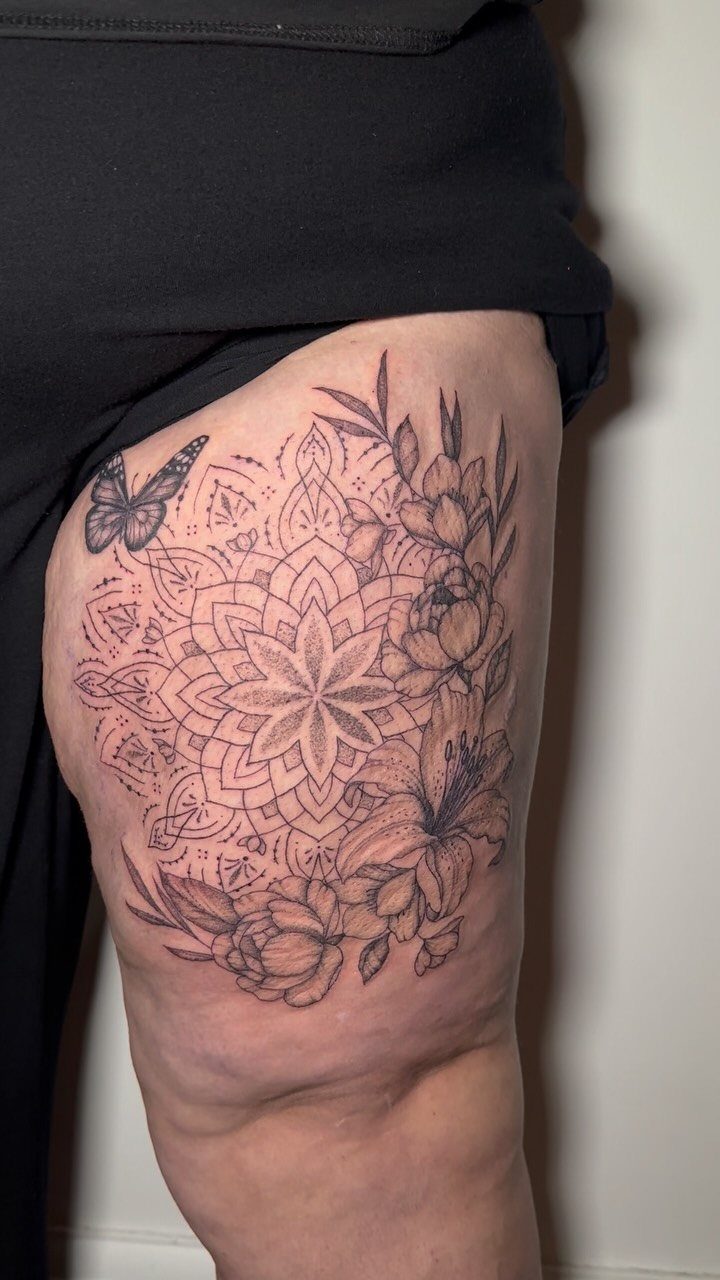 Mandala butterfly tattoo on a thigh with intricate floral patterns in black ink.