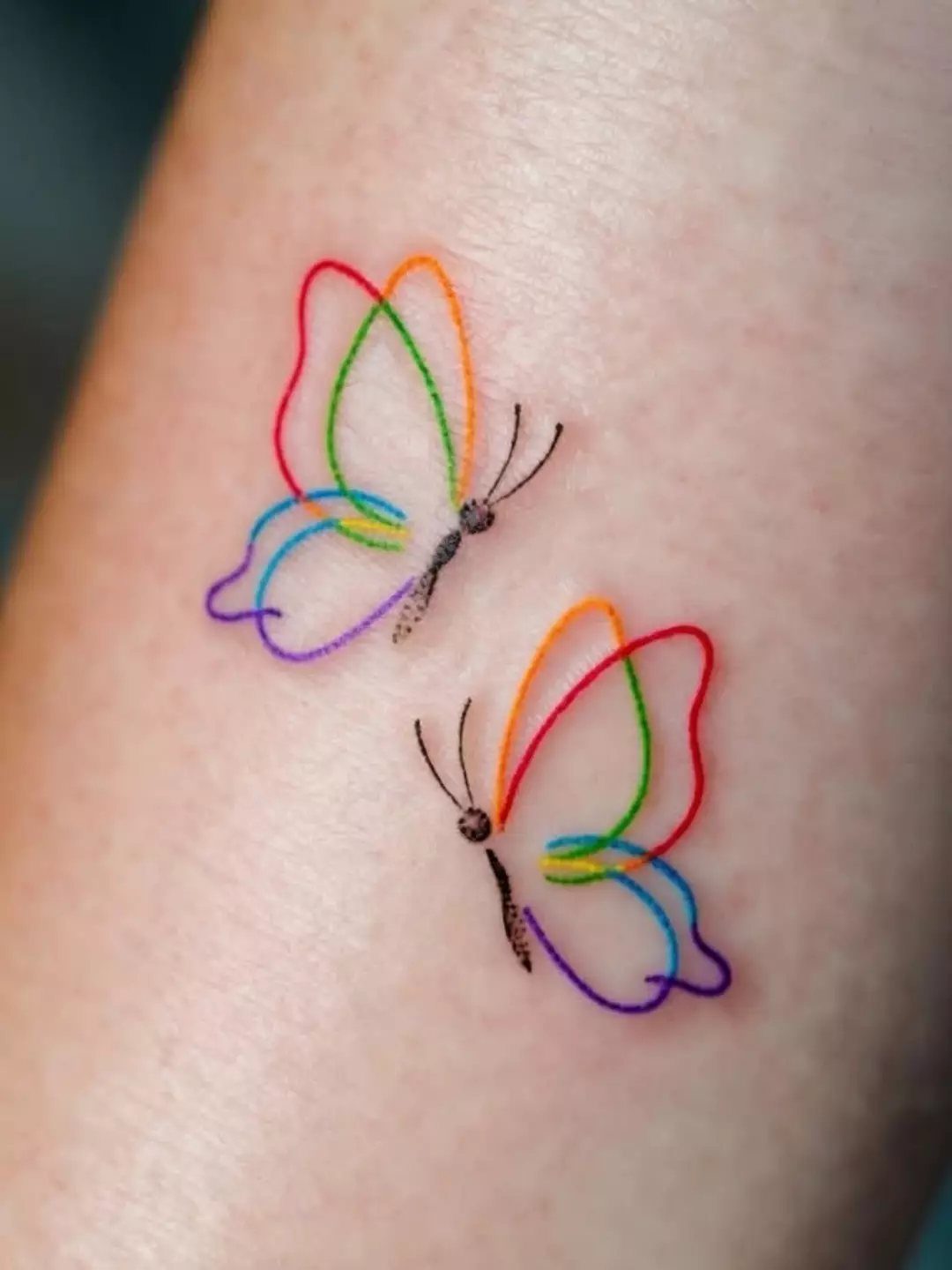 Two rainbow colored butterfly tattoos on a person's thigh skin.