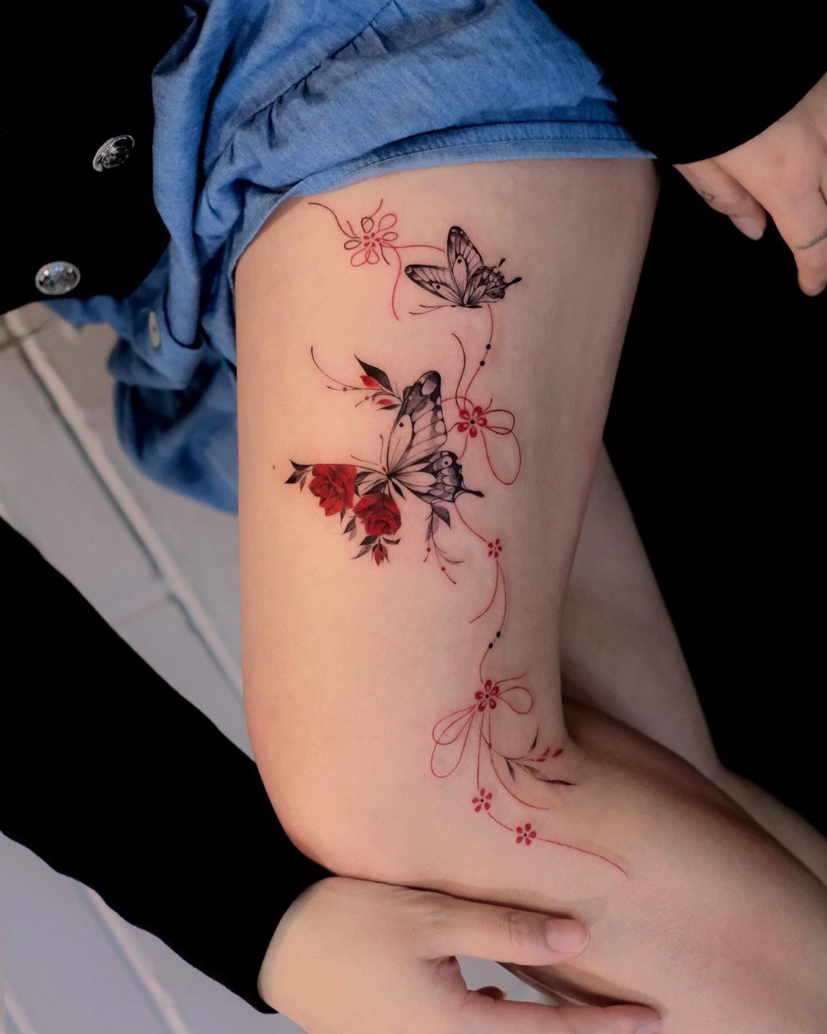Butterfly and flower tattoo with red and black ink on a person's thigh