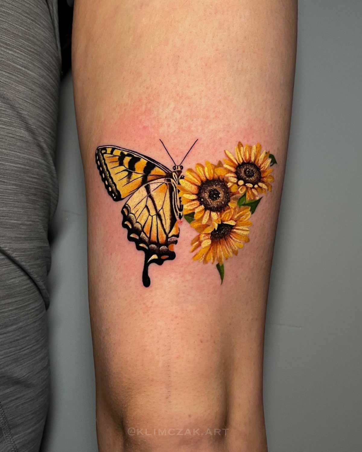 Yellow and black butterfly tattoo with three sunflowers on a person's thigh