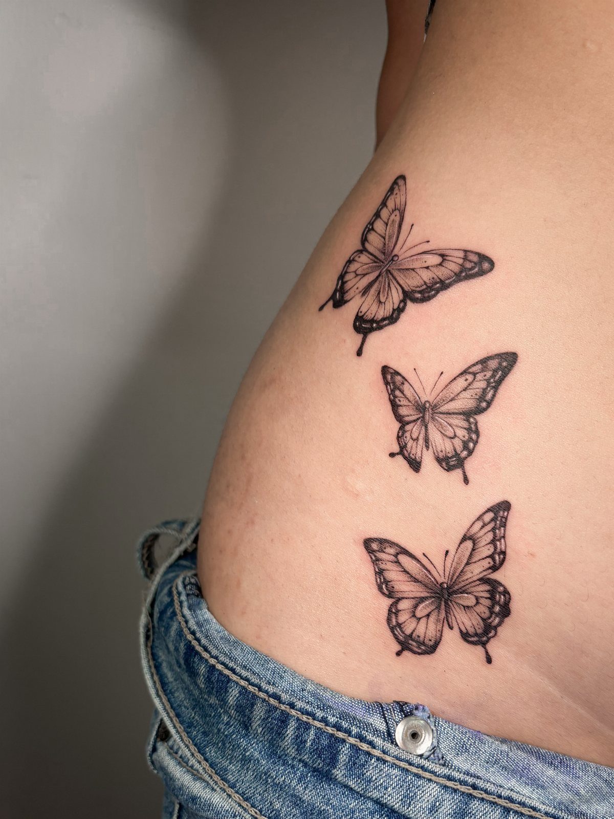 Three black butterfly tattoos arranged vertically on a person's upper thigh.