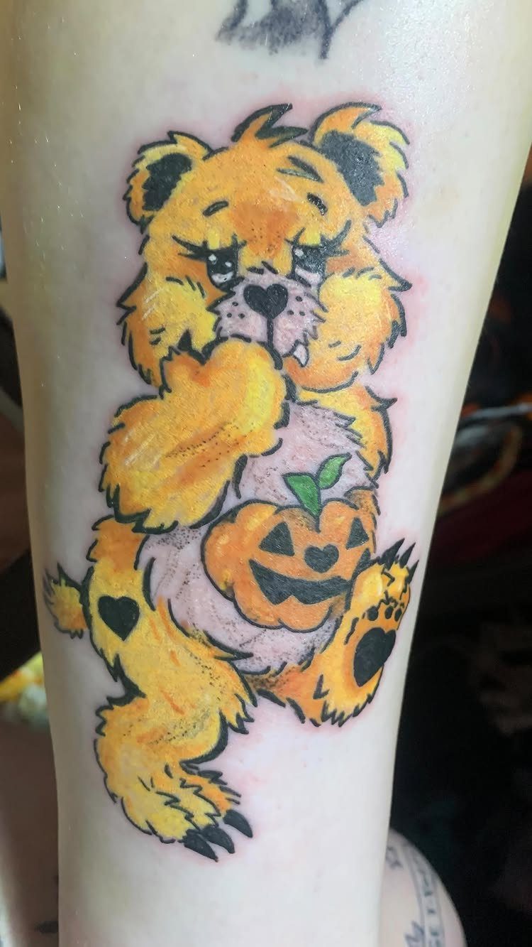 Yellow Care Bear tattoo holding a carved orange pumpkin on a person's leg