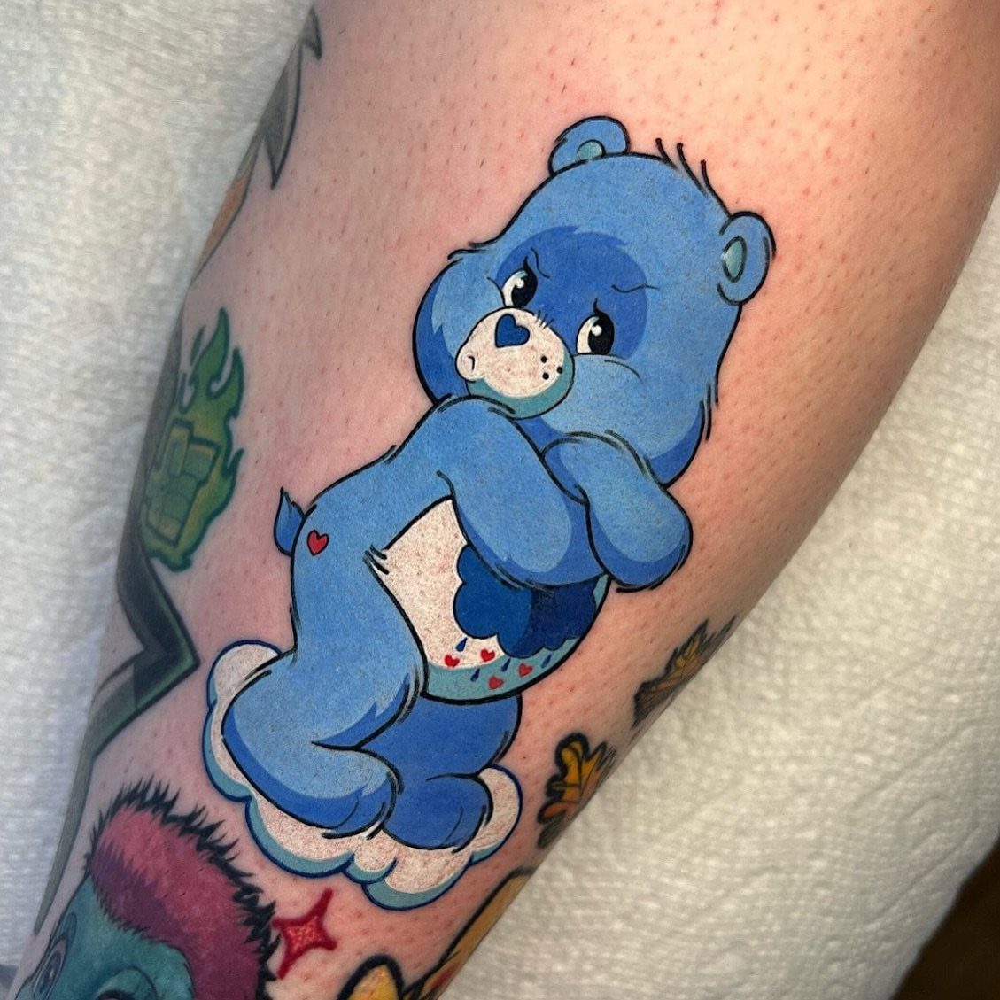 Blue Grumpy Bear tattoo with a frowning face and rain cloud belly.