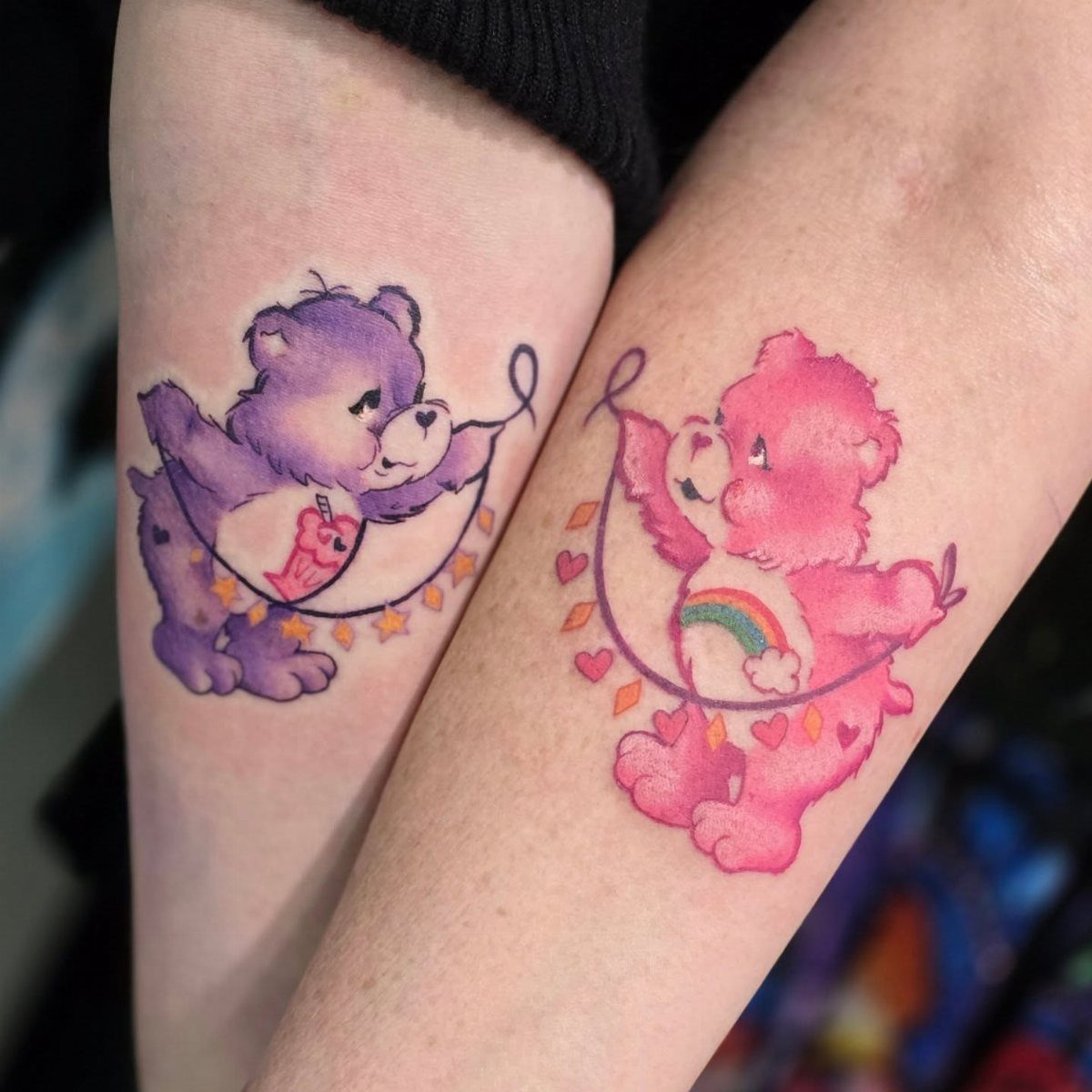 Two matching Care Bear tattoos on arms, one purple and one pink bear.