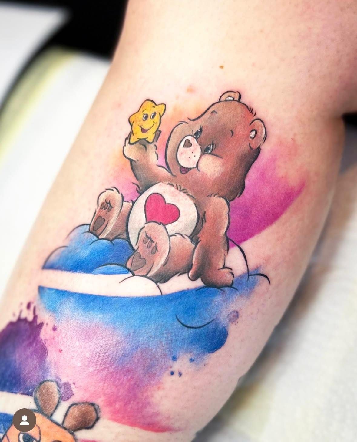 Brown Care Bear tattoo with a red heart and watercolor splashes on skin.
