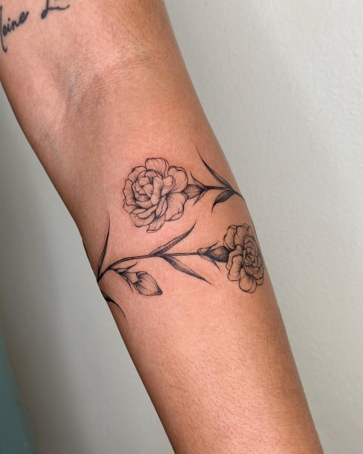 Black ink carnation flower tattoo with stems and leaves on a forearm