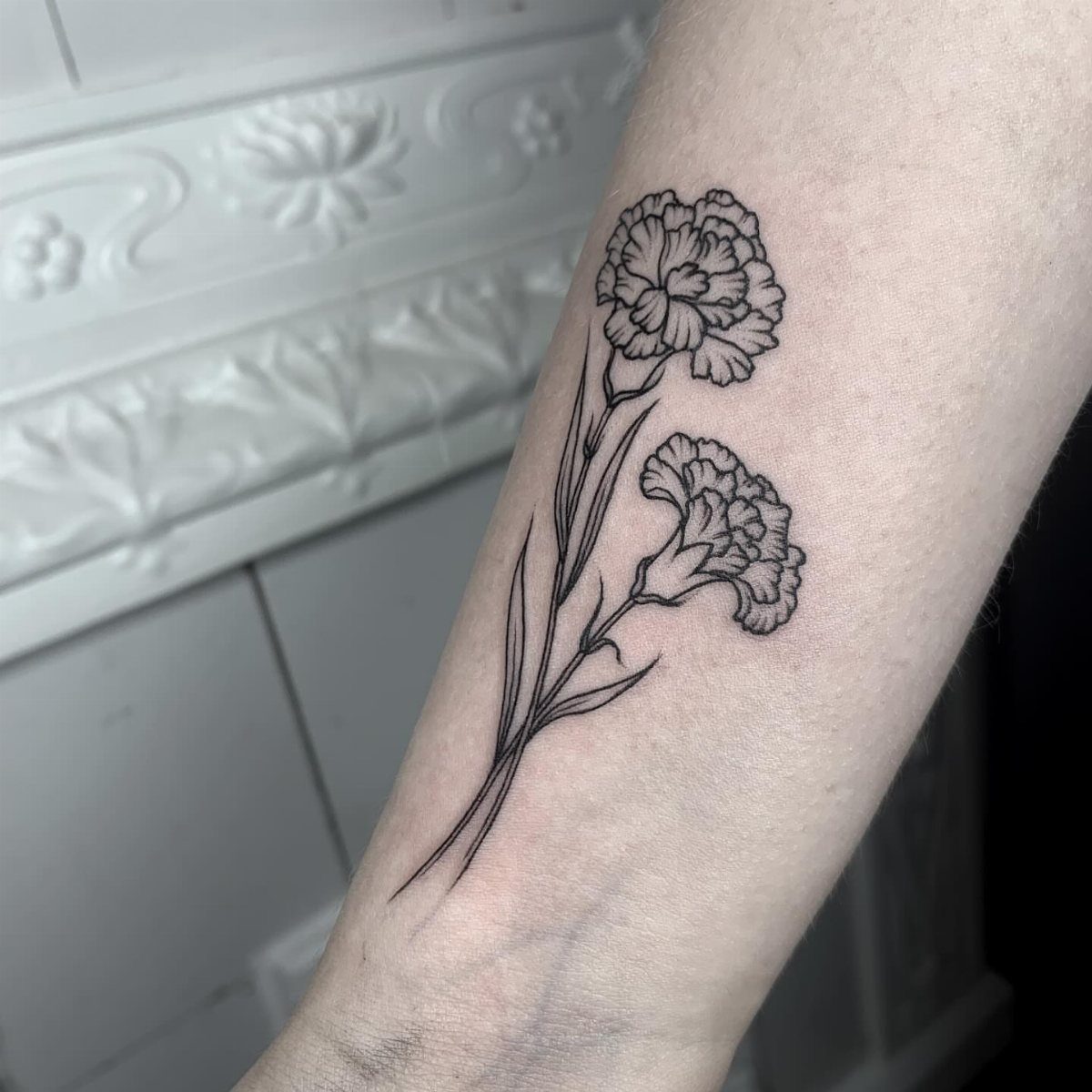 Black ink outline tattoo of two carnation flowers on a person's forearm