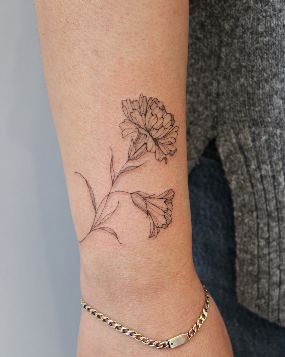 Carnation flower tattoo in black fine-line style on a person's inner wrist