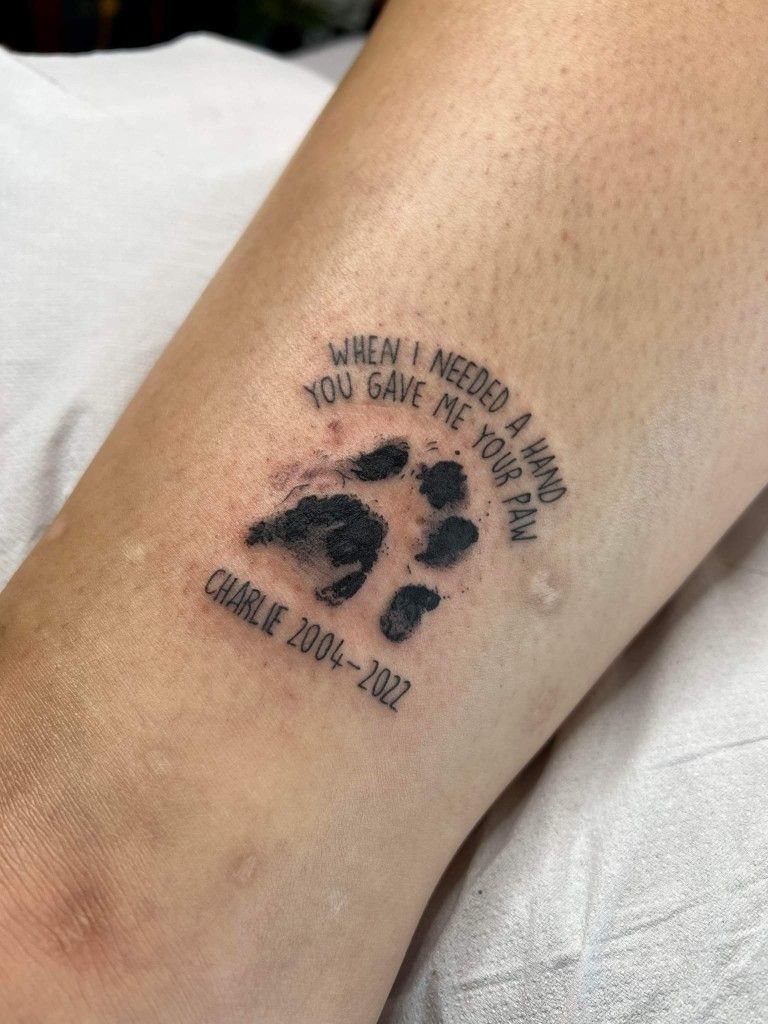 Realistic paw print tattoo with memorial text and years on a person's arm