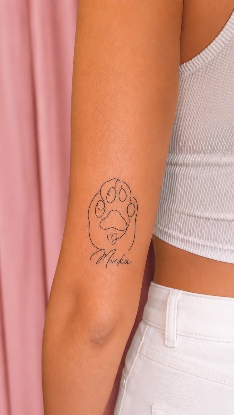 Cat paw print tattoo with a heart and the name Micka on an arm