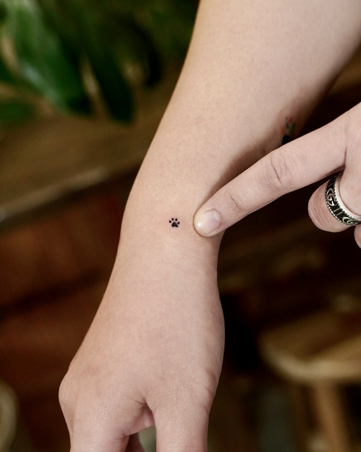 Small black cat paw print tattoo on a person's inner wrist.