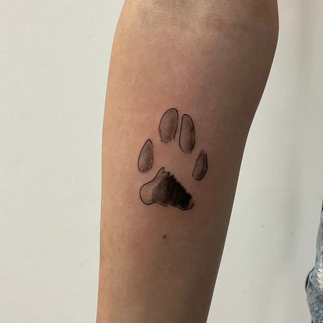 Cat paw print tattoo in black ink on a person's forearm.