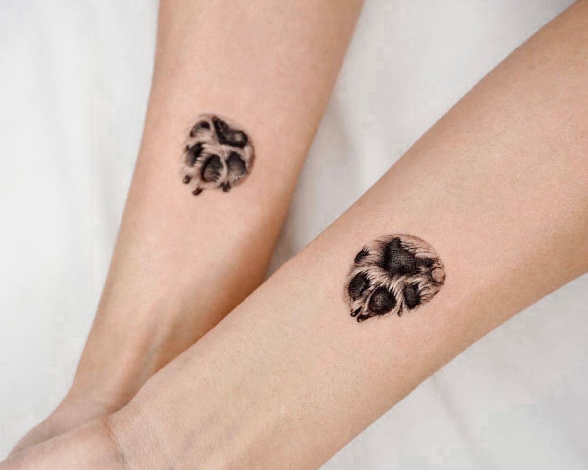 Two realistic cat paw tattoos with fur detail on two people's forearms.
