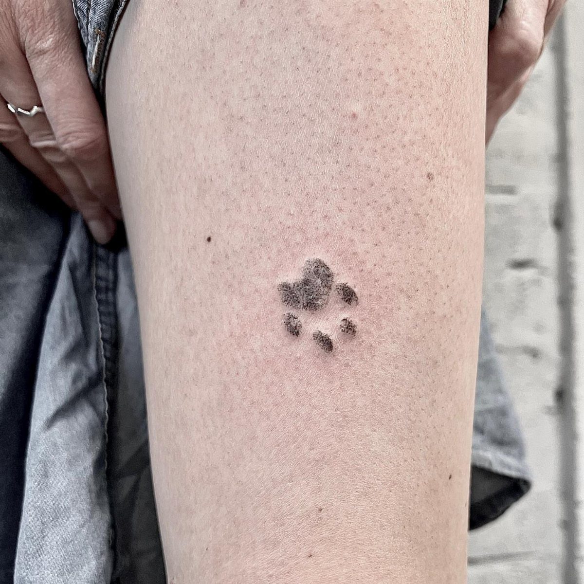 Small black cat paw print tattoo on a person's leg