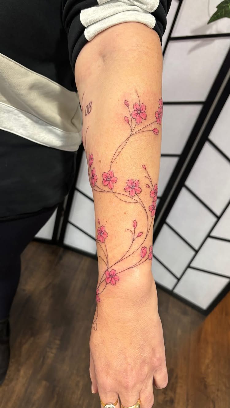 Pink cherry blossom tattoo with flowing vines wrapping around a person's forearm.
