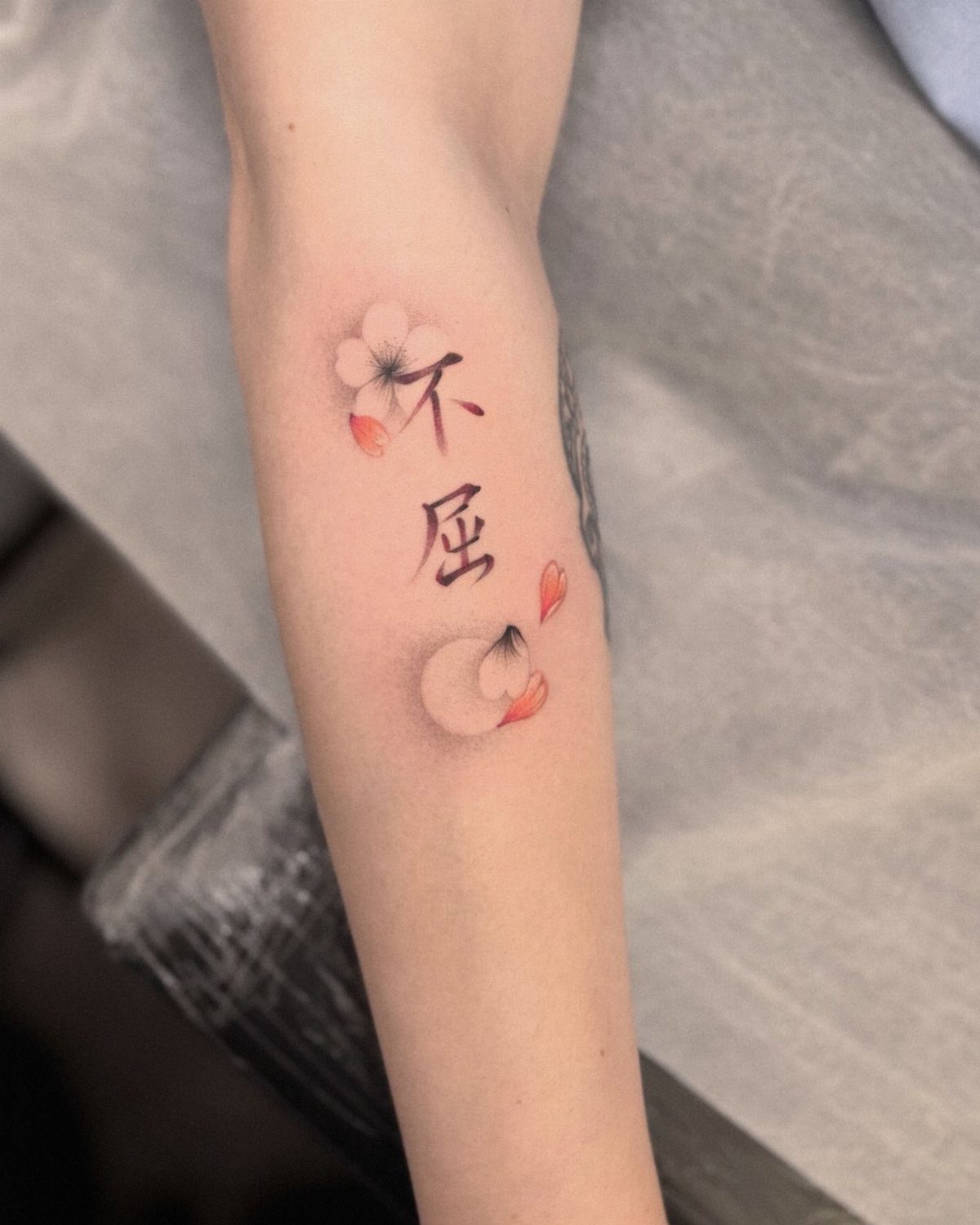 Cherry blossom tattoo with black kanji characters on a person's forearm