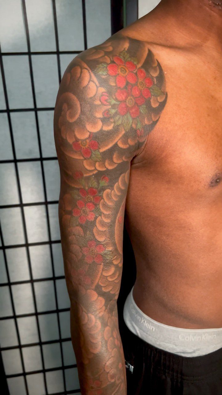Red cherry blossom tattoo on a man's shoulder and arm with grey clouds.
