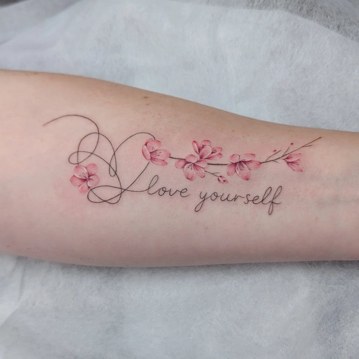 Cherry blossom tattoo with a heart and the words love yourself on forearm