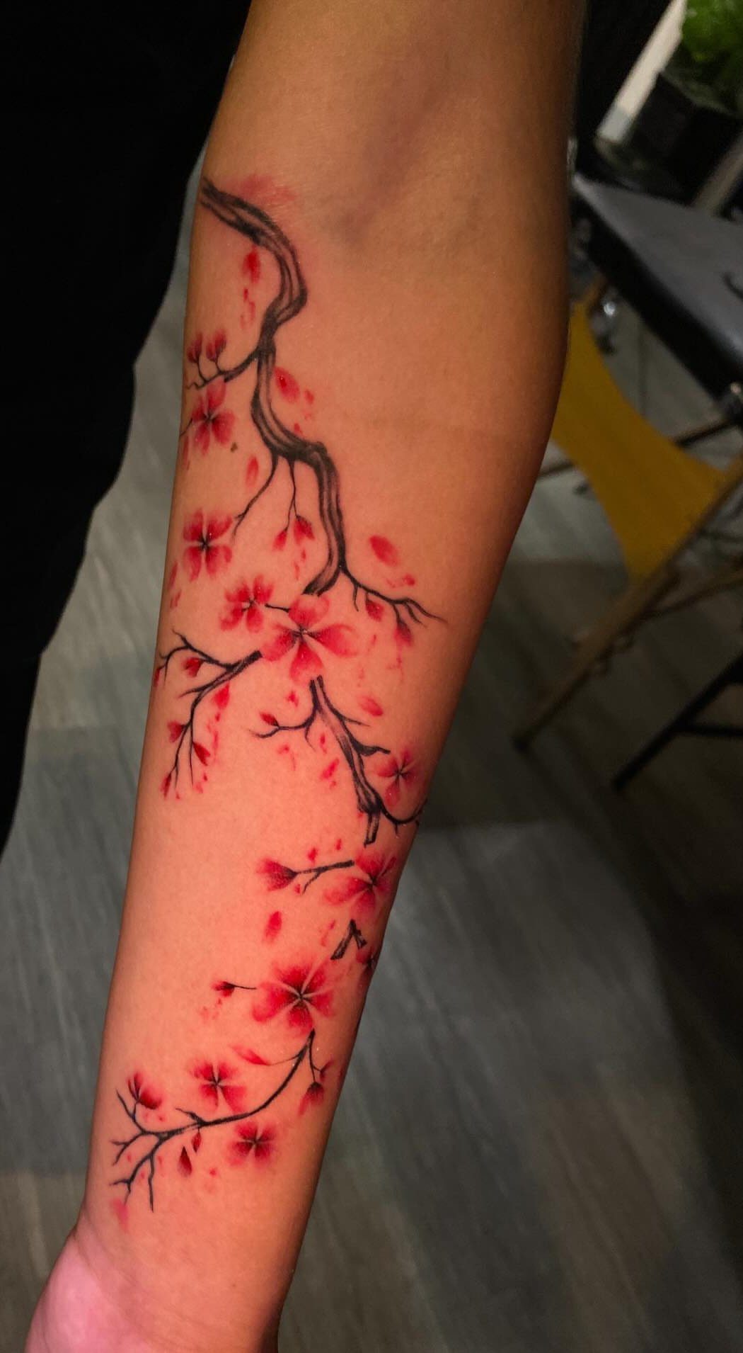 Red cherry blossom tattoo on a forearm with a dark brown branch.