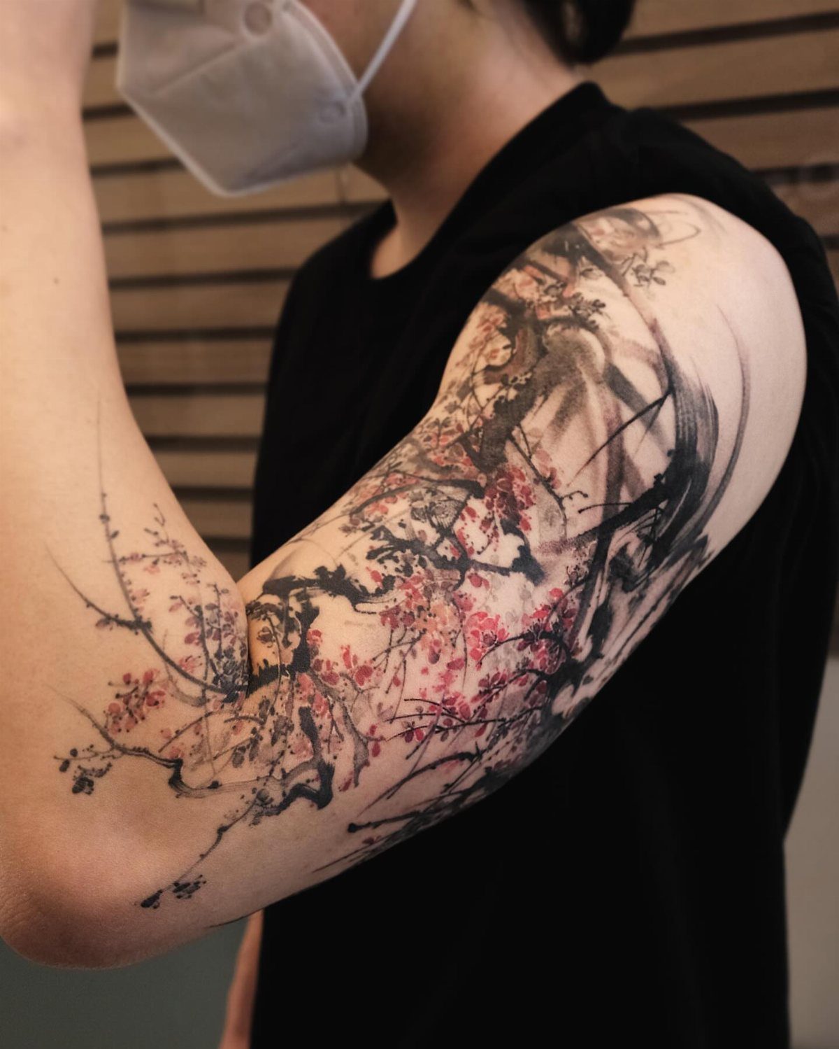 Cherry blossom tattoo with pink flowers and black ink on a person's arm