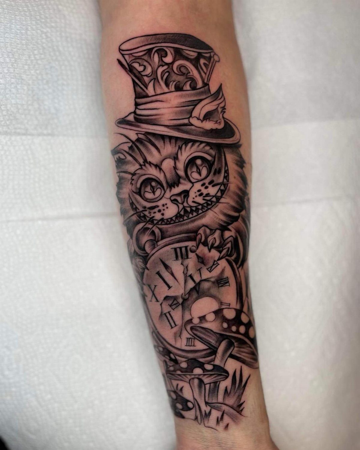 Cheshire Cat tattoo with a top hat, clock, and mushroom on a forearm