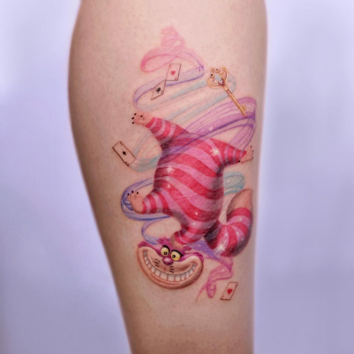 Cheshire Cat tattoo with pink stripes, floating cards, and a golden key.