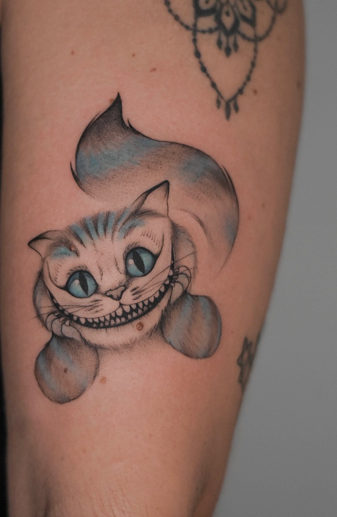 Cheshire Cat tattoo with a wide grin and blue eyes on human skin