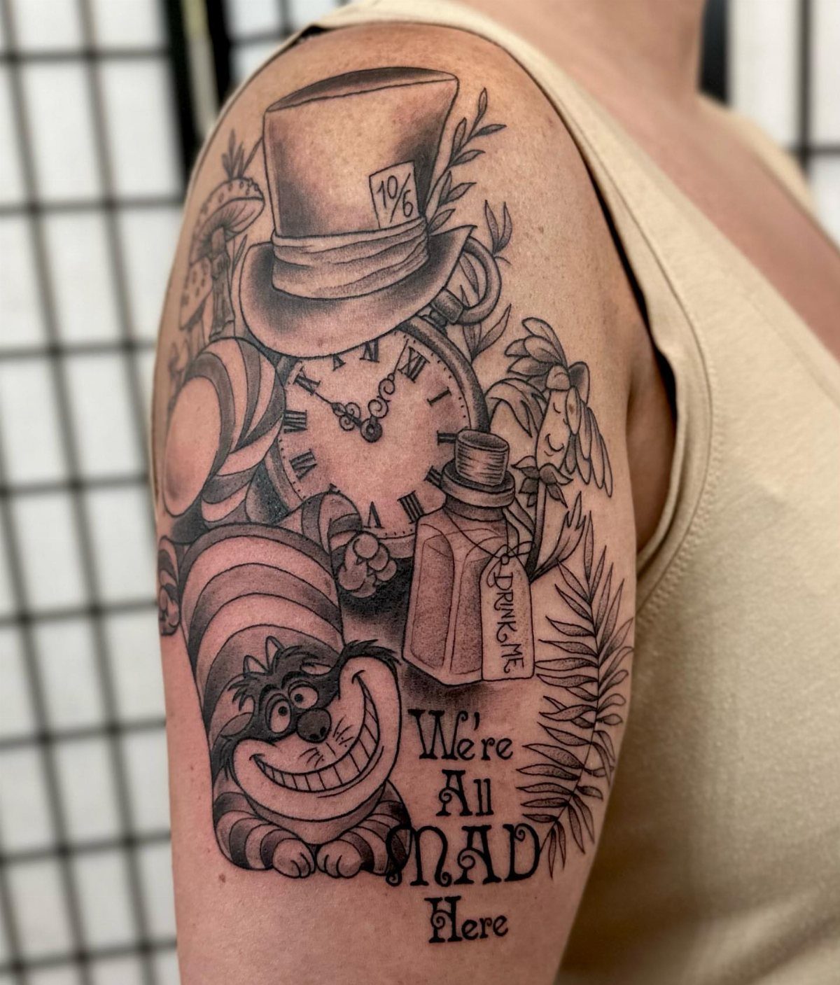 Cheshire Cat tattoo with top hat, clock, and 'We're All Mad Here' text.