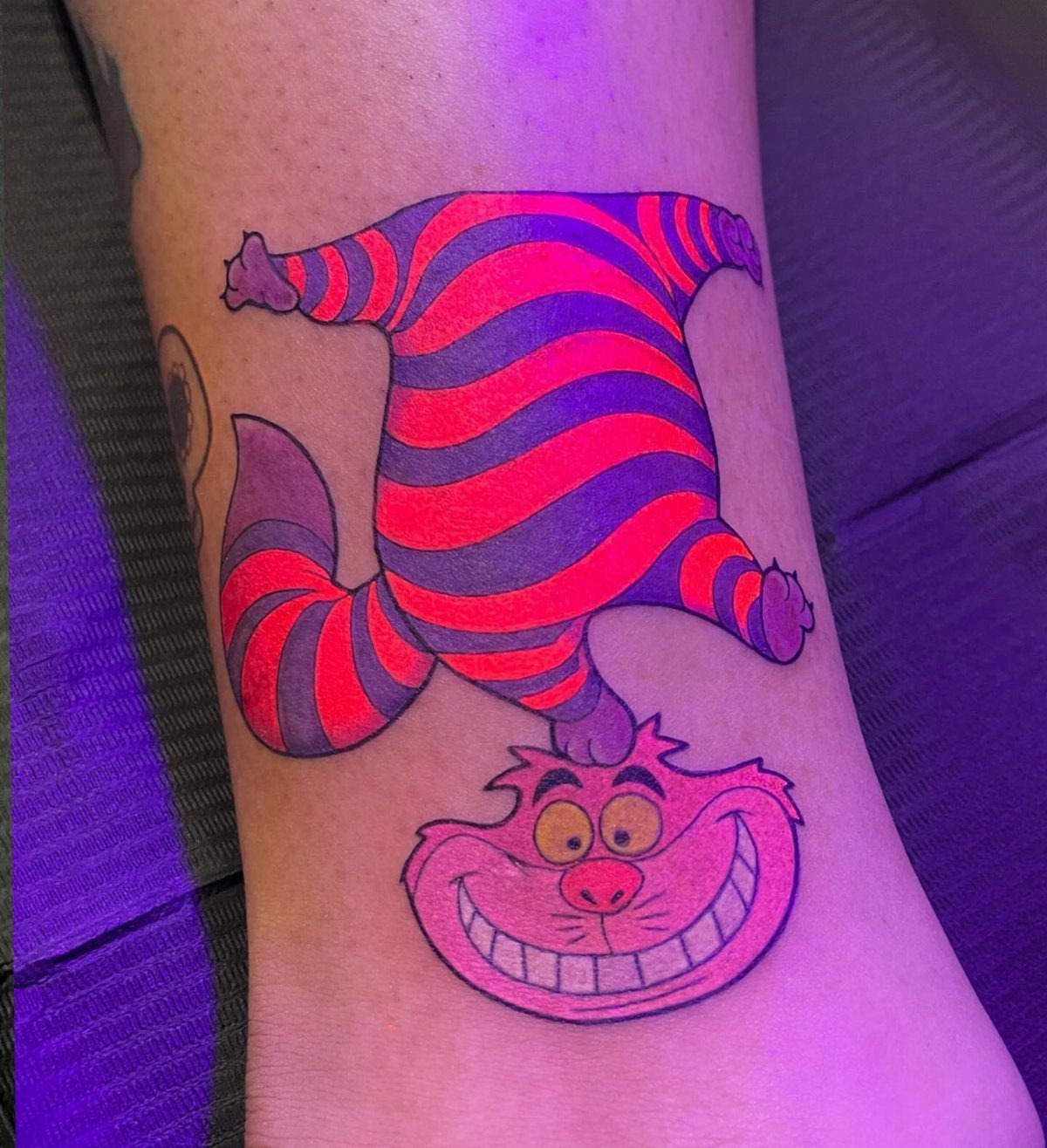 Cheshire Cat tattoo on an ankle with a wide grin and striped body.