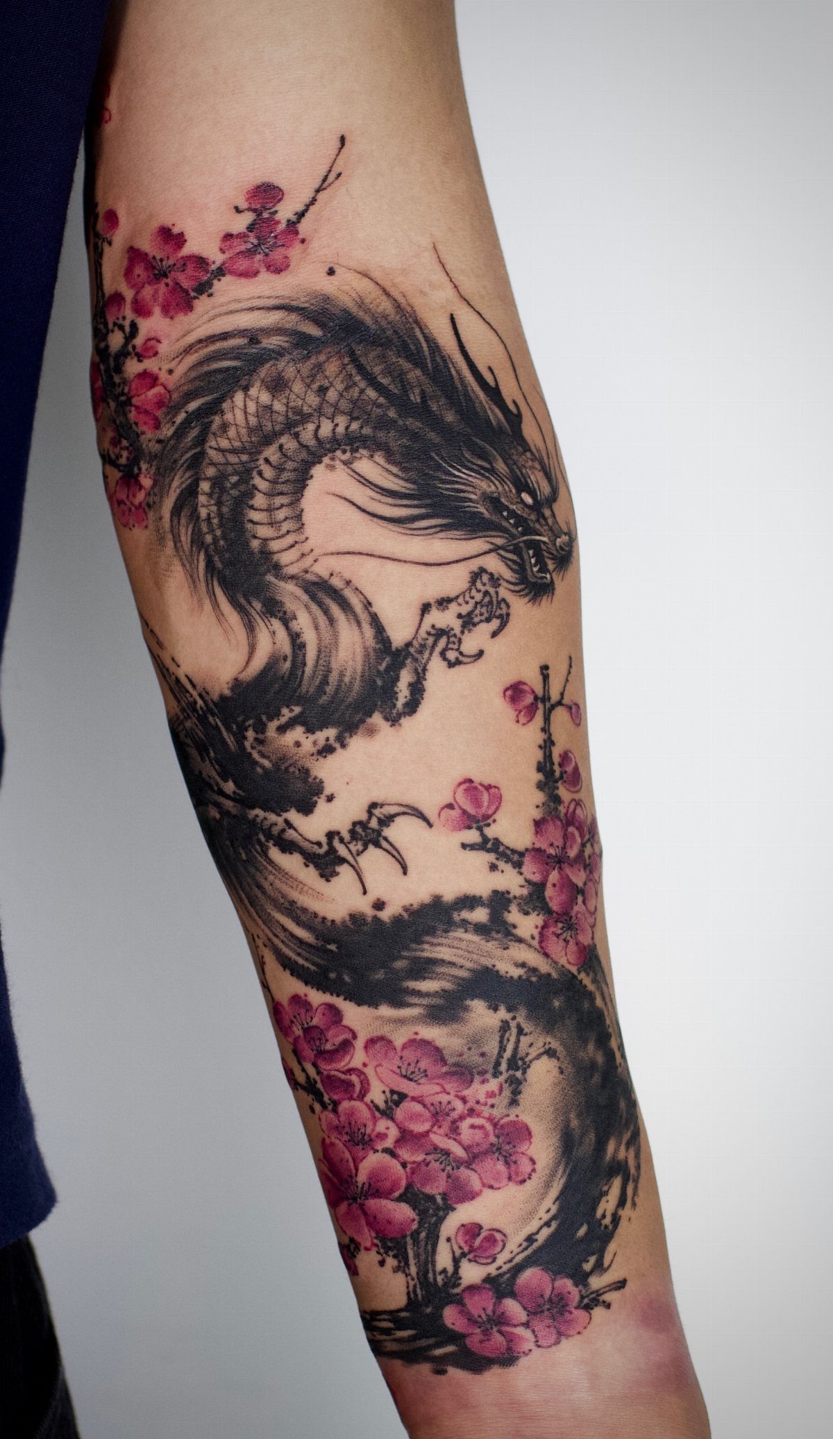Chinese dragon tattoo with pink cherry blossoms winding around a person's arm