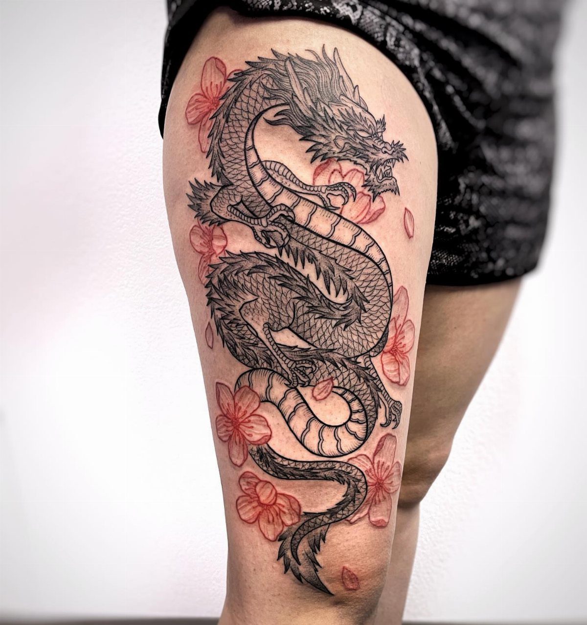 Chinese dragon tattoo with red cherry blossoms on a person's thigh