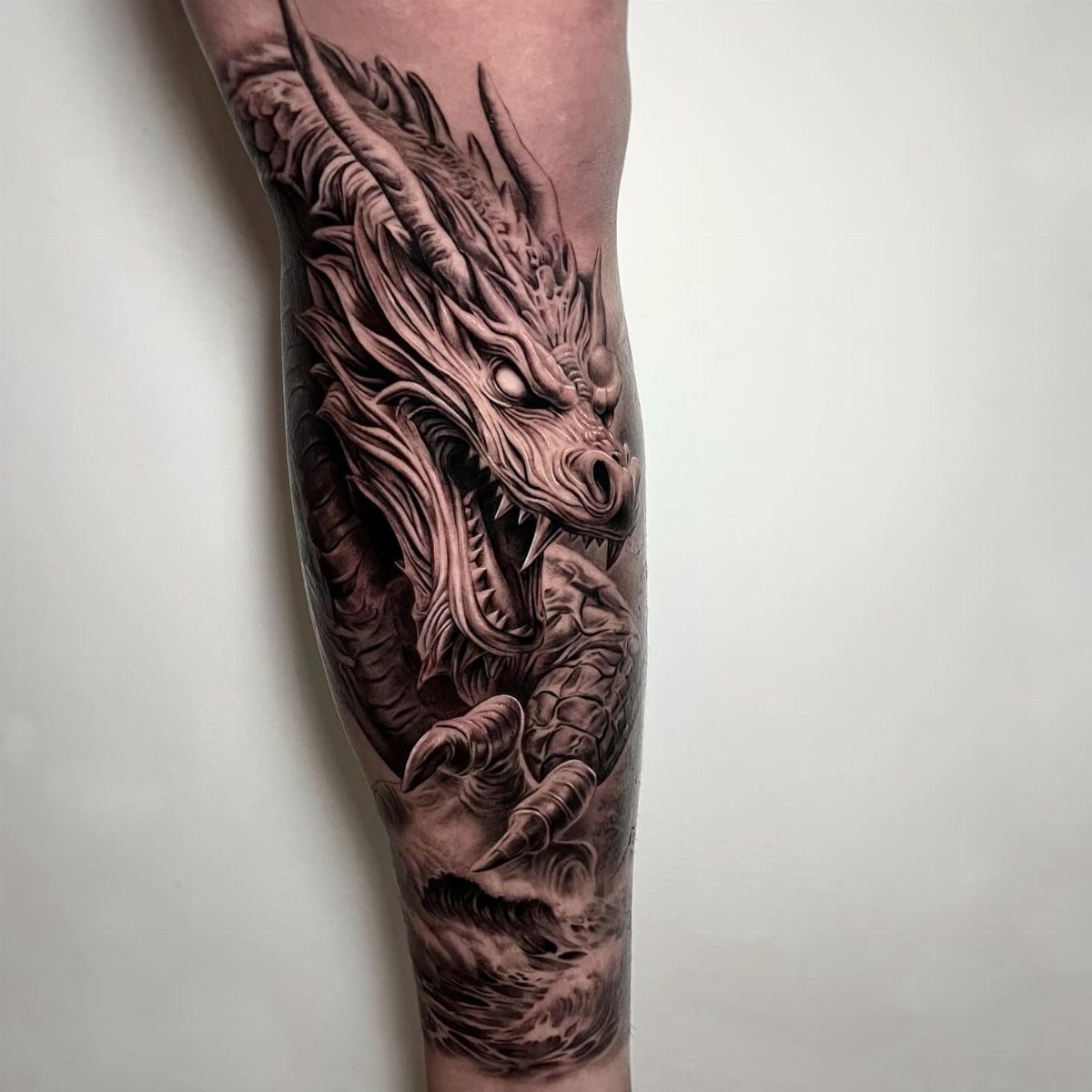 Detailed black and grey Chinese dragon tattoo on a person's forearm with clouds
