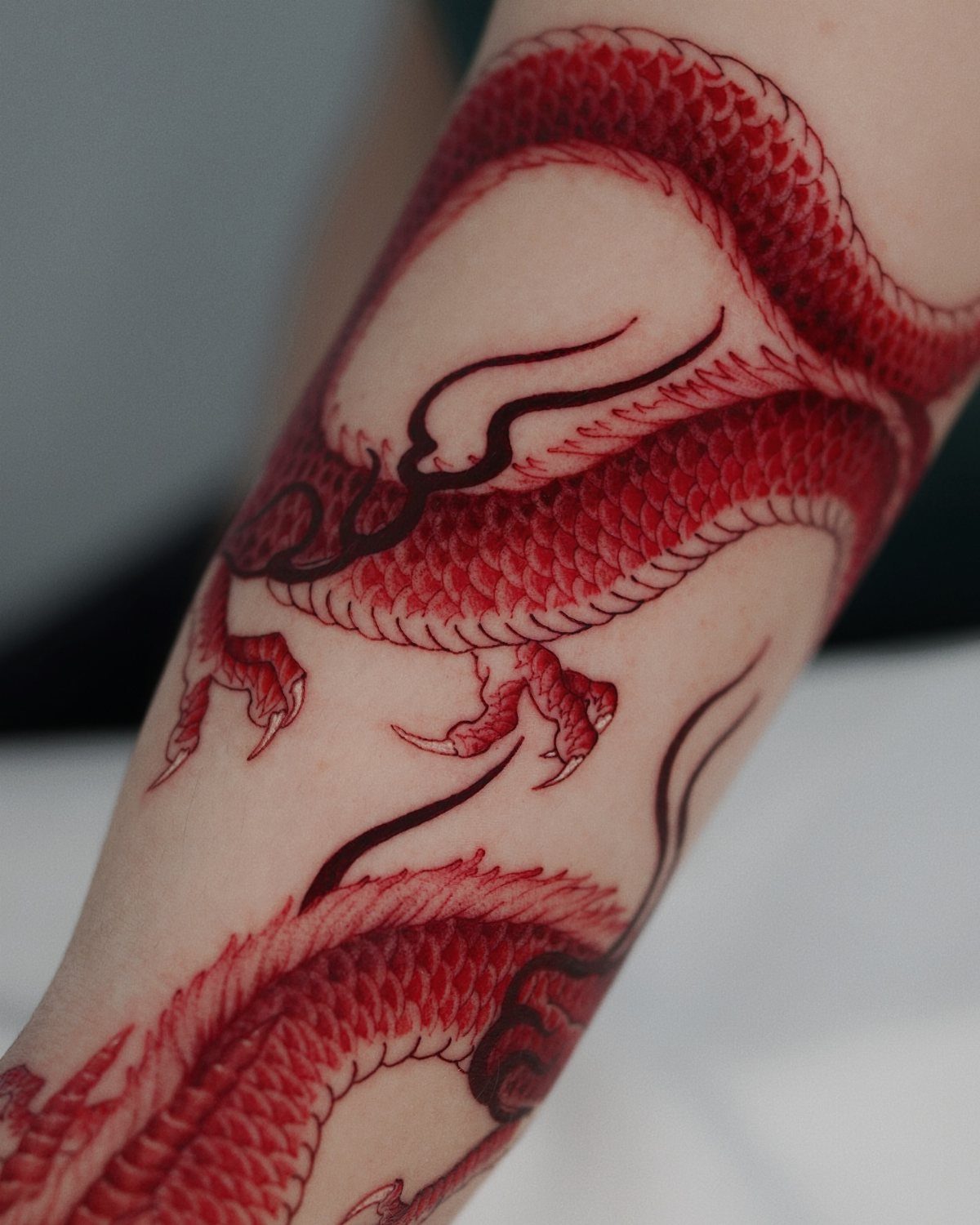 Red Chinese dragon tattoo with black outlines wrapped around a person's arm.