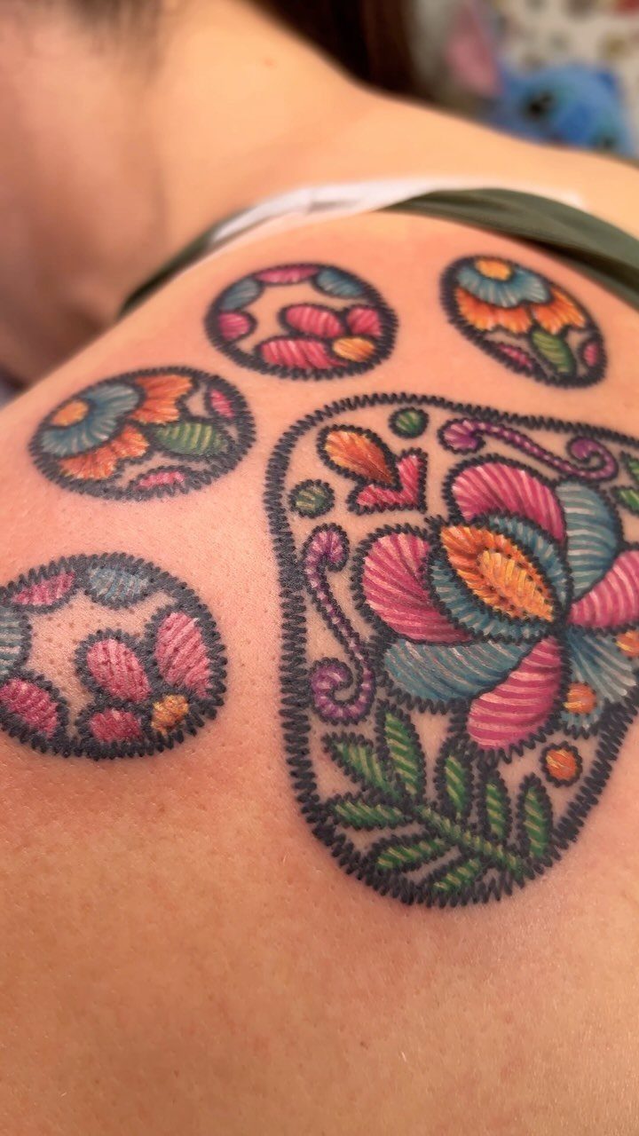 Colorful dog paw tattoo with floral embroidery style on a person's shoulder