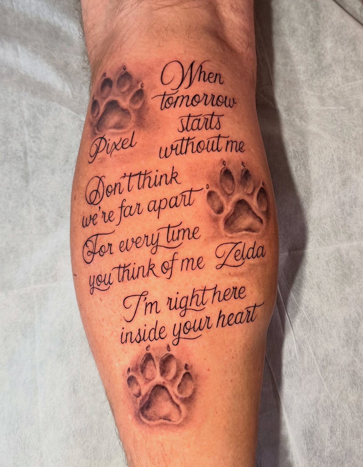 Dog paw tattoos with a memorial poem and names on a person's leg