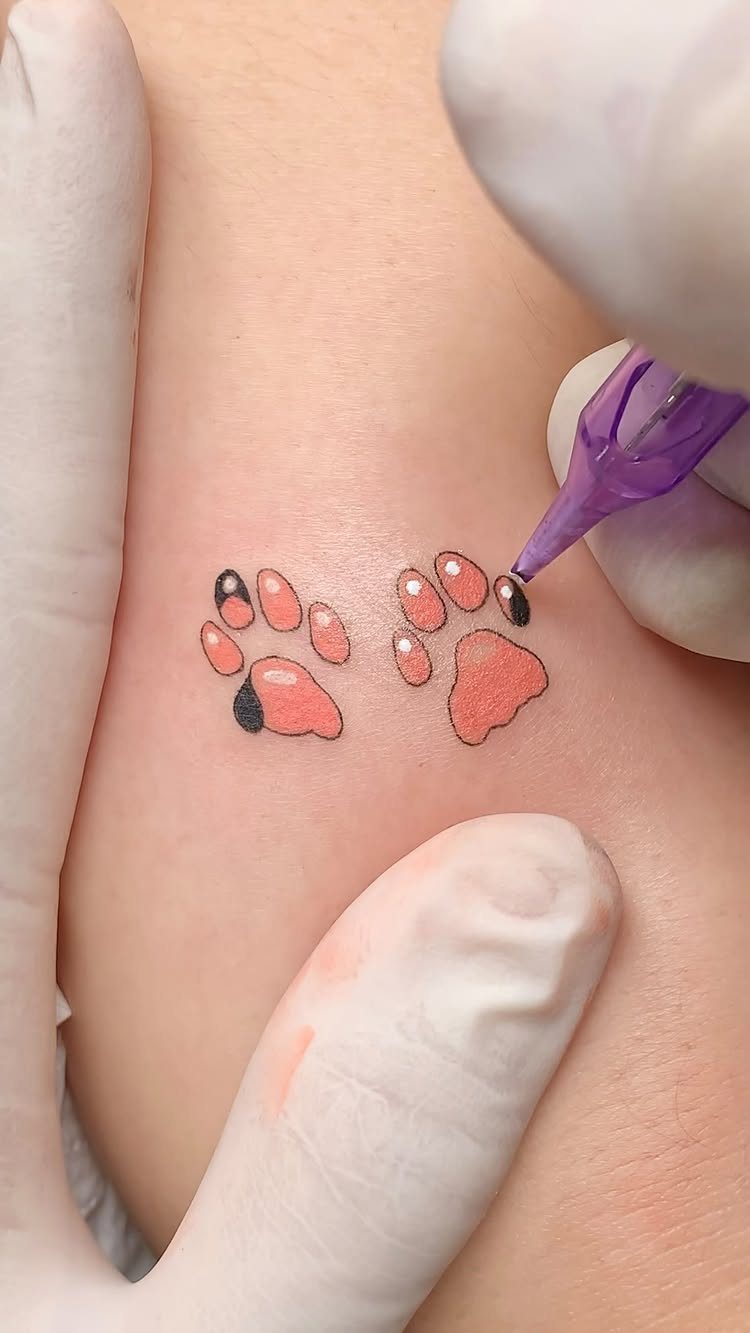 Two orange and black dog paw print tattoos being inked on skin.
